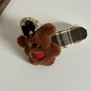 Détail de la pince à cheveux ours en peluche avec bonnet et cœur rouge sur fond gris