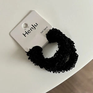 Elastic cream-style black textured hair ring set with brand tag on white background