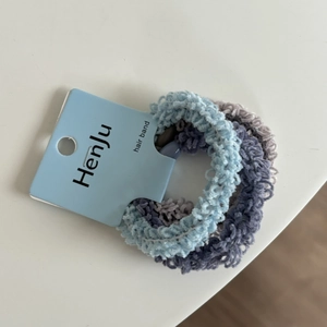 Detail view of plush chenille hair ties in blue, purple, and grey with a brand tag