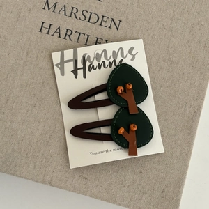 Detail of two handmade leather tree hair clips with orange beads on a vintage book