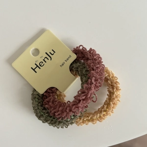 Detail of three-piece set of cream-colored elastic hair ties in rose, olive and beige