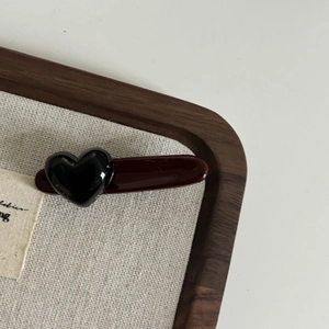 Macro shot of minimalist wine red hairpin with glossy black heart resin detail