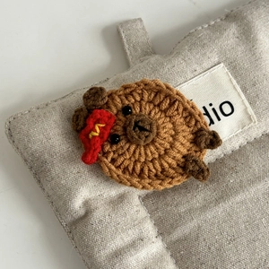 Nahaufnahme einer handgestrickten Bären-Haarklammer mit rotem Anhänger und Wolltextur