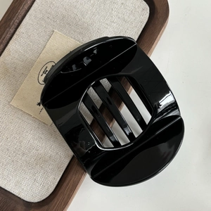 Macro detail of large black acrylic hair claw with glossy finish on a wooden tray