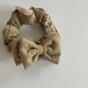 Close-up of khaki scrunchie in plain weave fabric with a sweet bow logo on a white label