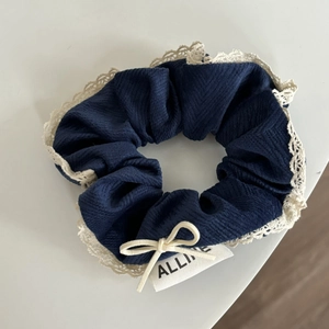 Detail of dark blue lace scrunchie with delicate cream bow and woven brand tag