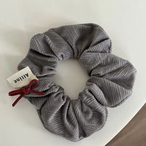 Detailed shot of grey corduroy scrunchie featuring a small red ribbon bow and woven label
