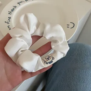 Detail showing the soft white satin scrunchie with a cute woven label and elegant pleats