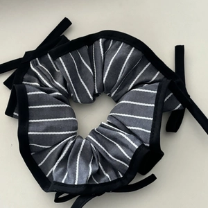 Detailed view of grey and white striped fabric scrunchie with black ribbons and piping