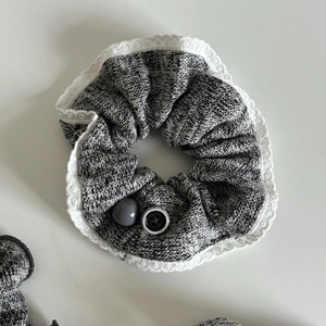 Détail d'un chouchou en tricot gris avec bordure en dentelle, bouton noir et perle