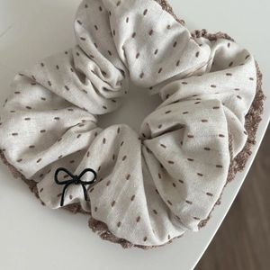Detail of beige scrunchie with brown embroidery, crochet edge and bow charm