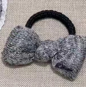 Détail d'un chouchou noeud en tricot gris avec texte brodé sur fond en toile de jute