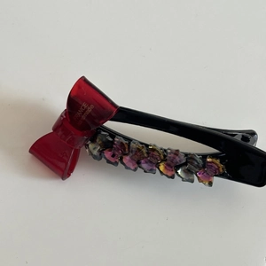 Detailaufnahme der handgefertigten roten Haarklammer mit lila Blumen und Schleifen-Design