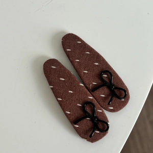 Detailed view of brown fabric hair clips with white stitching and black bow accents