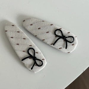 Detail of cream cotton linen hair clips with brown stitching and black bow accents