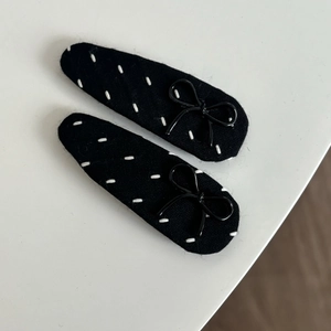 Close-up of black fabric snap hair clips with white embroidery and glossy bows