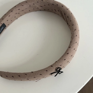 Detailed macro view of a brown padded fabric headband with dark embroidery and metal bow
