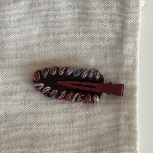 Close-up of handmade woven hair clip with multi-color yarn on red metal duckbill base