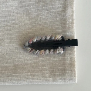 Detail of hand-woven colorful wool yarn covering a black duckbill hair clip base