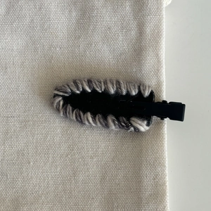 Close-up of woven French acetate hair clip with gray and white yarn on white linen background