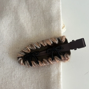 Close-up of woven acetate hair clip with brown yarn trim and two black bow details
