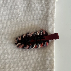 Detail of woven fabric hair clip with red and navy threads and black bows decoration