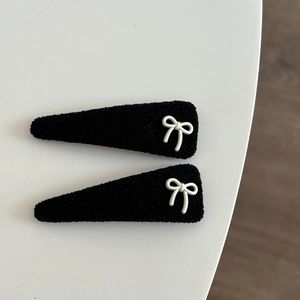 Detail of black velvet hair clips with white bow accents on a minimalist white table