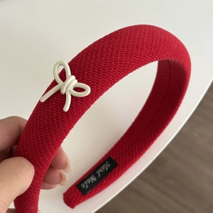 Detail of red knitted headband with a cream bow and Hand Made woven label detail