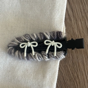 Detail of hand-woven grey wool hair clip with white bows on a black base clip