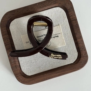 Détail d'une pince à cheveux marron chocolat avec lettrage doré sur tissu texturé