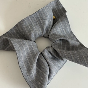 Detail of grey striped fabric scrunchie featuring a decorative gold circular button accent