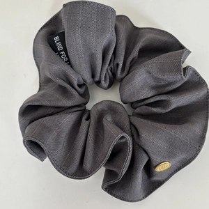 Detail of dark grey striped fabric scrunchie with Blind For Love label and golden metal charm