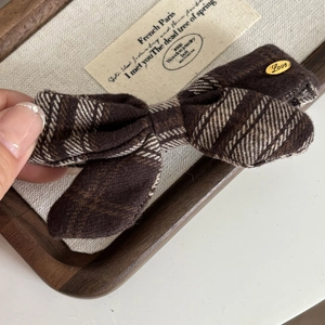 Detailed view of the brown plaid bow hair clip with an engraved golden Love metal tag