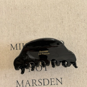 Detail of glossy black acetate hair claw clip featuring gold La France engraving on fabric