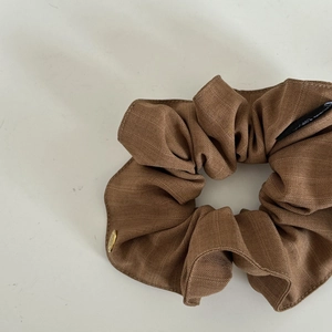 Detailed close-up of brown striped fabric scrunchie with a gold logo and woven label