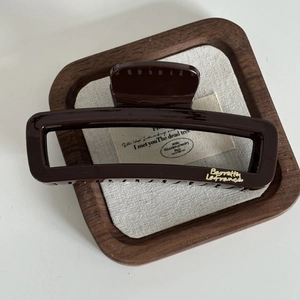 Détail d'une pince à cheveux carrée marron chocolat avec lettrage doré sur plateau bois