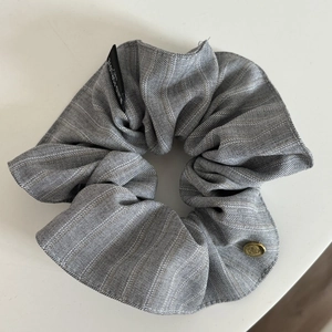 Detailed view of grey striped fabric scrunchie with gold metal plate and woven label