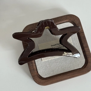 Détail d'une pince à cheveux étoile marron foncé avec accents dorés sur plateau en bois