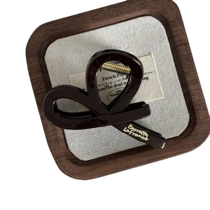 Pince à cheveux géométrique marron chocolat avec étiquette dorée sur plateau en bois