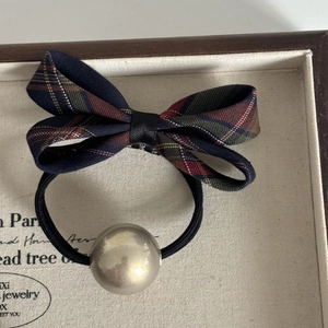 Detail of navy blue plaid bow hair tie with champagne gold bead on wooden tray