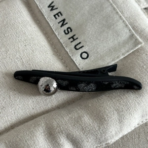 Brown leopard bow hair clip with silver ball detail on minimalist matte black surface