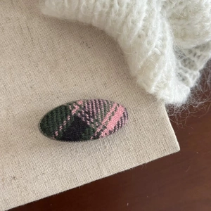 Detail of pink and green tartan fabric texture on an oval-shaped vintage hair clip