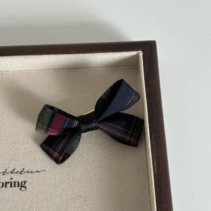 Detailed close-up of navy blue plaid bow hair clip on a vintage wooden tray