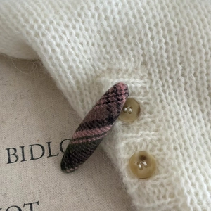 Detailed view of a pink plaid hair clip attached to a white knit fabric with brown buttons