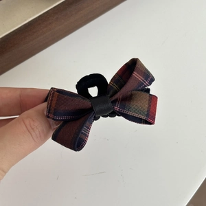 Close-up of a hand holding a classic red and green plaid bow hair clip with a fabric texture