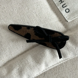 Detailed close-up of leopard print bow hair clip with textured fabric on rustic linen