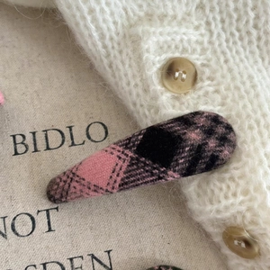 Close-up of a pink and black checkered tweed hair clip on a soft textured background