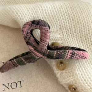 Detail of pink and green plaid tweed hair claw clip on white knitted sweater fabric