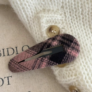 Close-up of vintage pink plaid fabric wrapped metal BB hair clip on a white knit background