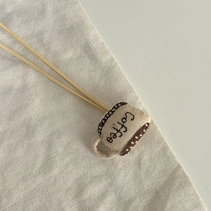 Détail du pendentif en tissu café fait main avec broderie Coffee sur fond en lin